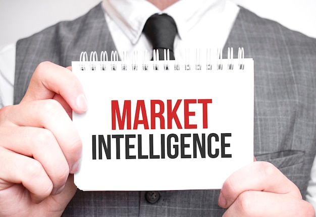 Um empresário segurando um bloco de notas que exibe o texto 'Market Intelligence', com uma expressão concentrada enquanto parece estar analisando informações.
