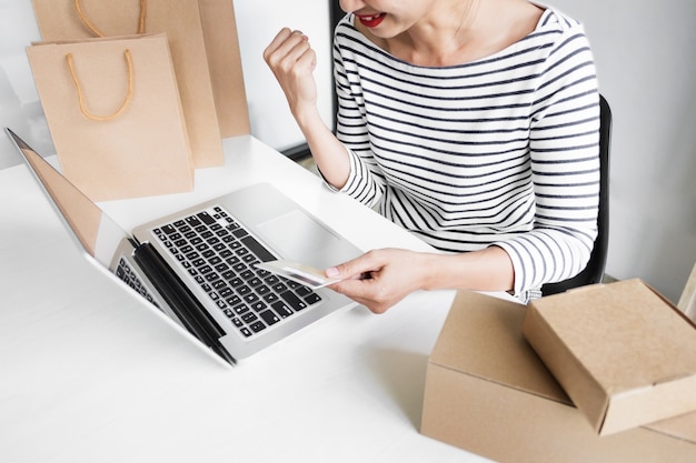 Close-up de uma jovem mulher feliz usando um notebook em casa, segurando um cartão de crédito enquanto insere as informações do seu cartão para compras online.