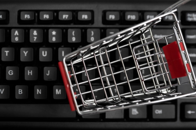 Vista de perto de um pequeno carrinho de compras colocado sobre um teclado, simbolizando as compras online.