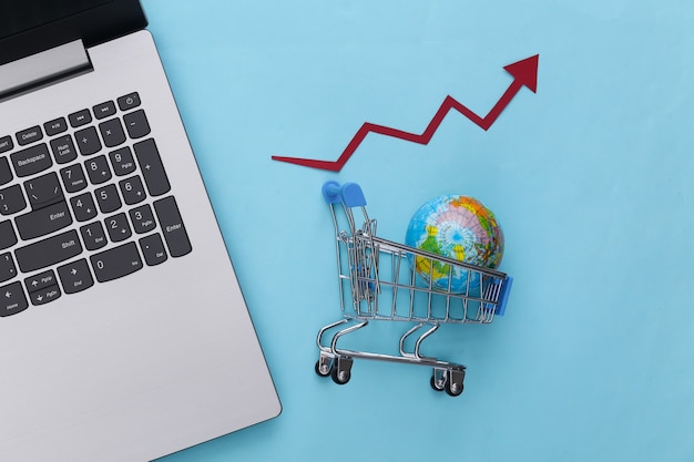 Um laptop e um carrinho de supermercado contendo um globo, com uma seta de crescimento apontando para cima contra um fundo azul, simbolizando o aumento das compras globais.
