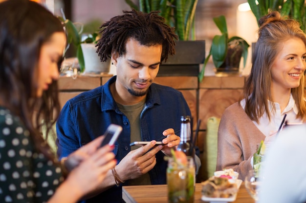 Um grupo de amigos sentados à mesa de um restaurante, cada um usando seu smartphone enquanto desfrutam de uma refeição juntos.
